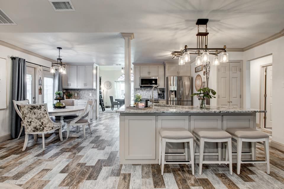 Open-concept kitchen with island and dining area; light wood floors, gray cabinets, stainless steel appliances, and beige walls.