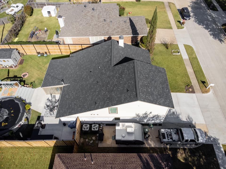 Overhead view of a house with a dark gray shingle roof, yard, and adjacent houses.