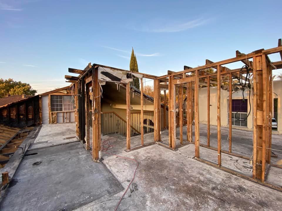 House undergoing renovation, showing exposed wooden framing and partial demolition of walls and roof.