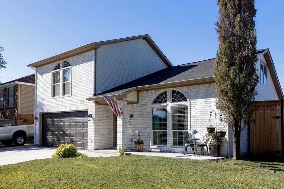 White brick house with a dark garage door, arched windows, and a front lawn.