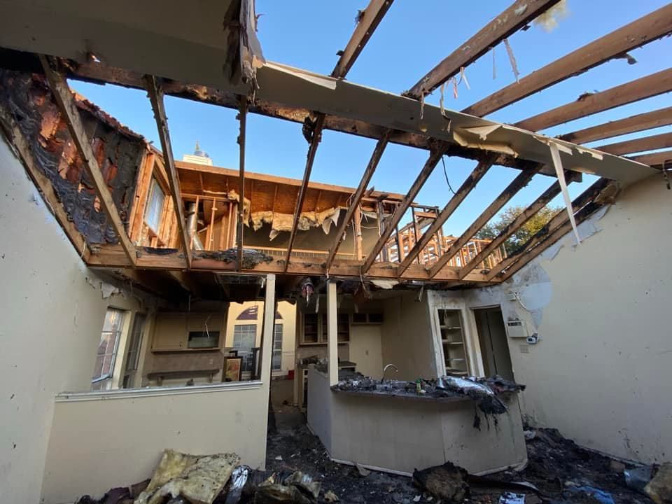 Interior of a house destroyed by fire; roof collapsed, walls and debris blackened.