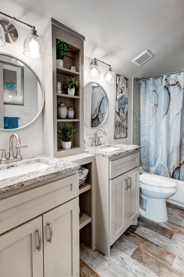 Bathroom with dual sinks, a central storage unit, and a shower with a blue marble patterned curtain.