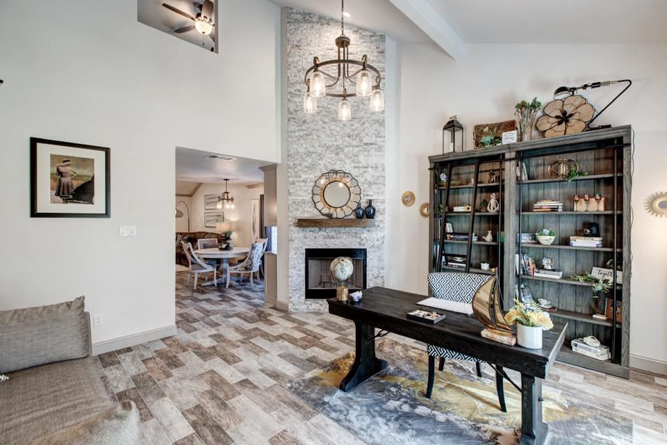 Spacious office with rustic decor, fireplace, large wooden desk, and bookshelf. View into dining room.