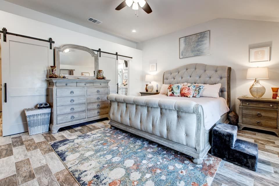 Spacious bedroom with grey dresser, tufted bed, colorful rug, and two sliding barn doors.
