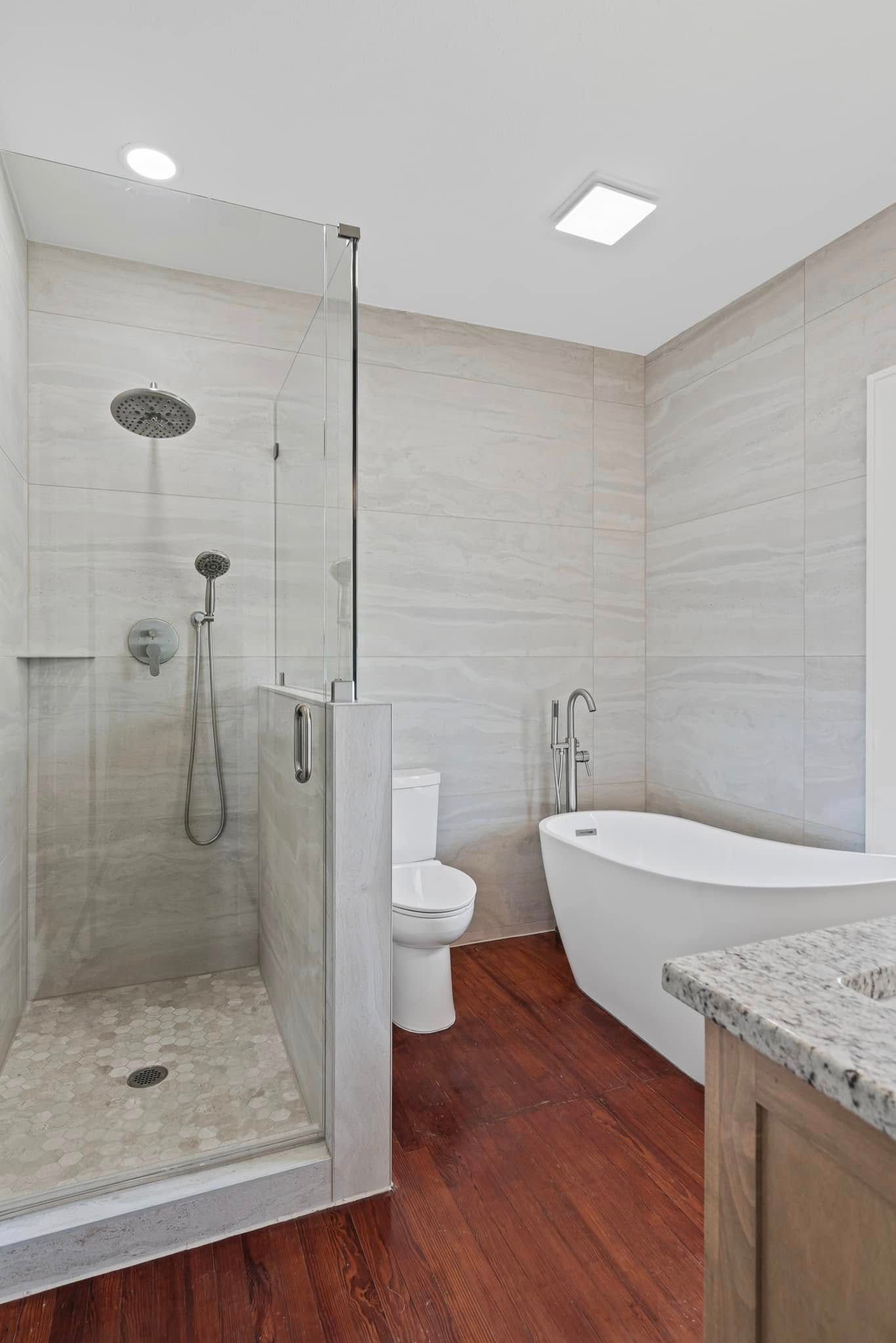 Modern bathroom with shower, toilet, and freestanding tub; light-colored tile, dark wood floor.