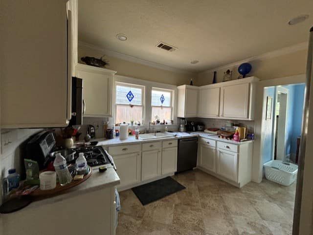 White kitchen with cabinets, stove, sink, and open doorway to another room.