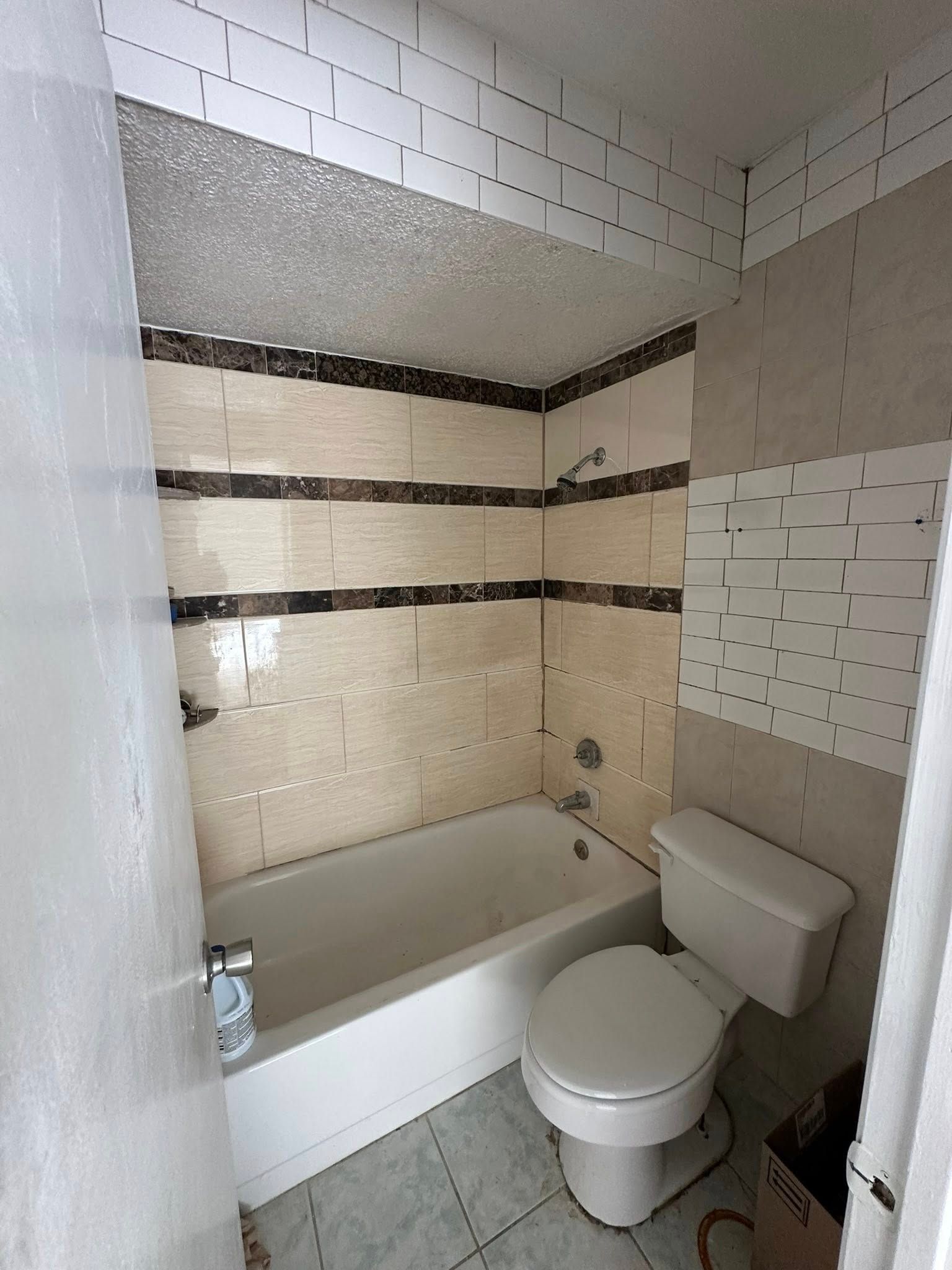Bathroom with tub, toilet, and tiled walls. Beige and brown tiles; white ceiling and tub.