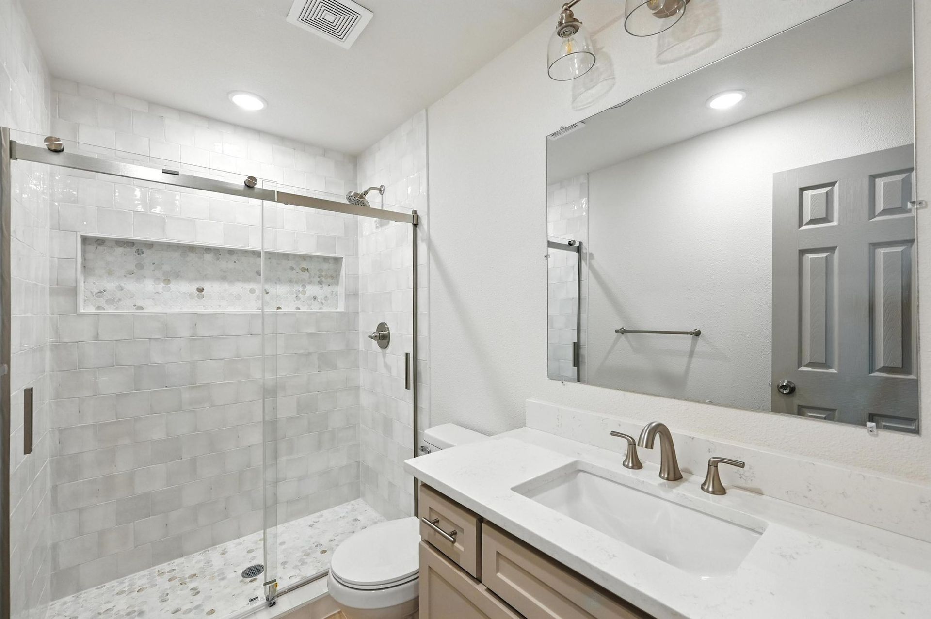 Modern bathroom with glass shower, white vanity, and neutral tile.