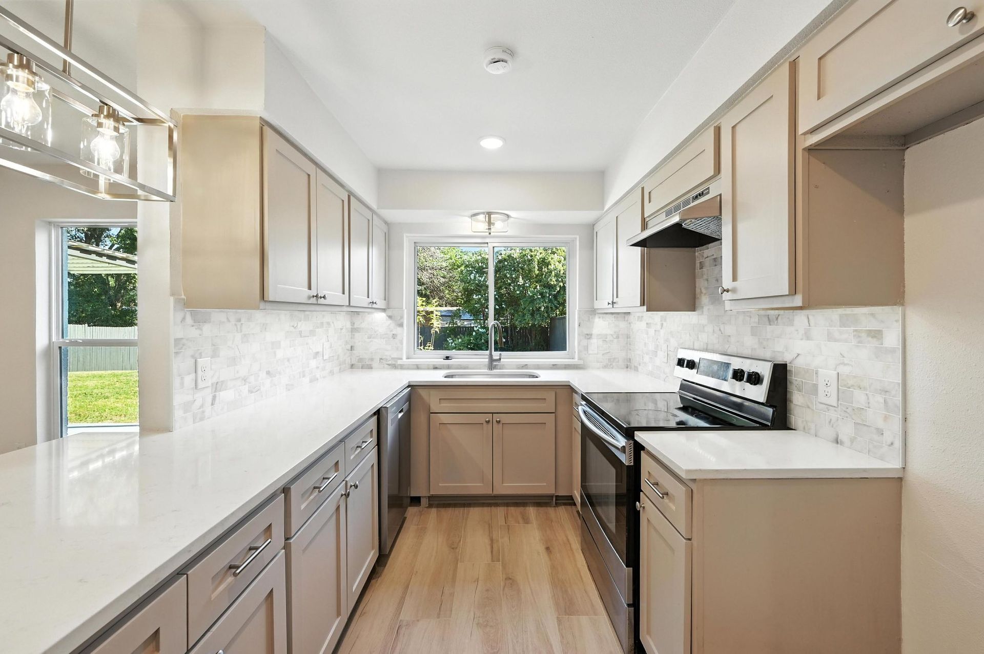 Modern kitchen with light wood cabinets, white countertops, and stainless steel appliances.