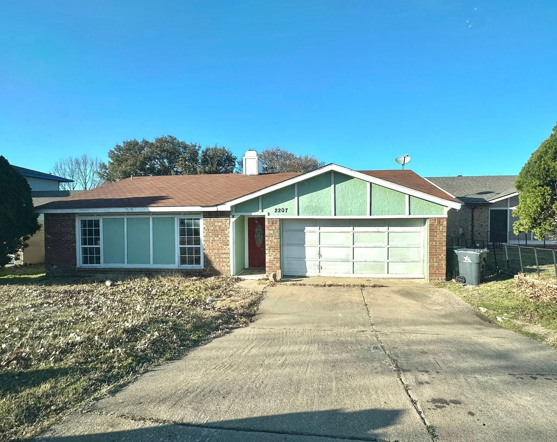A single-story brick house with a green gable and a driveway on a sunny day.