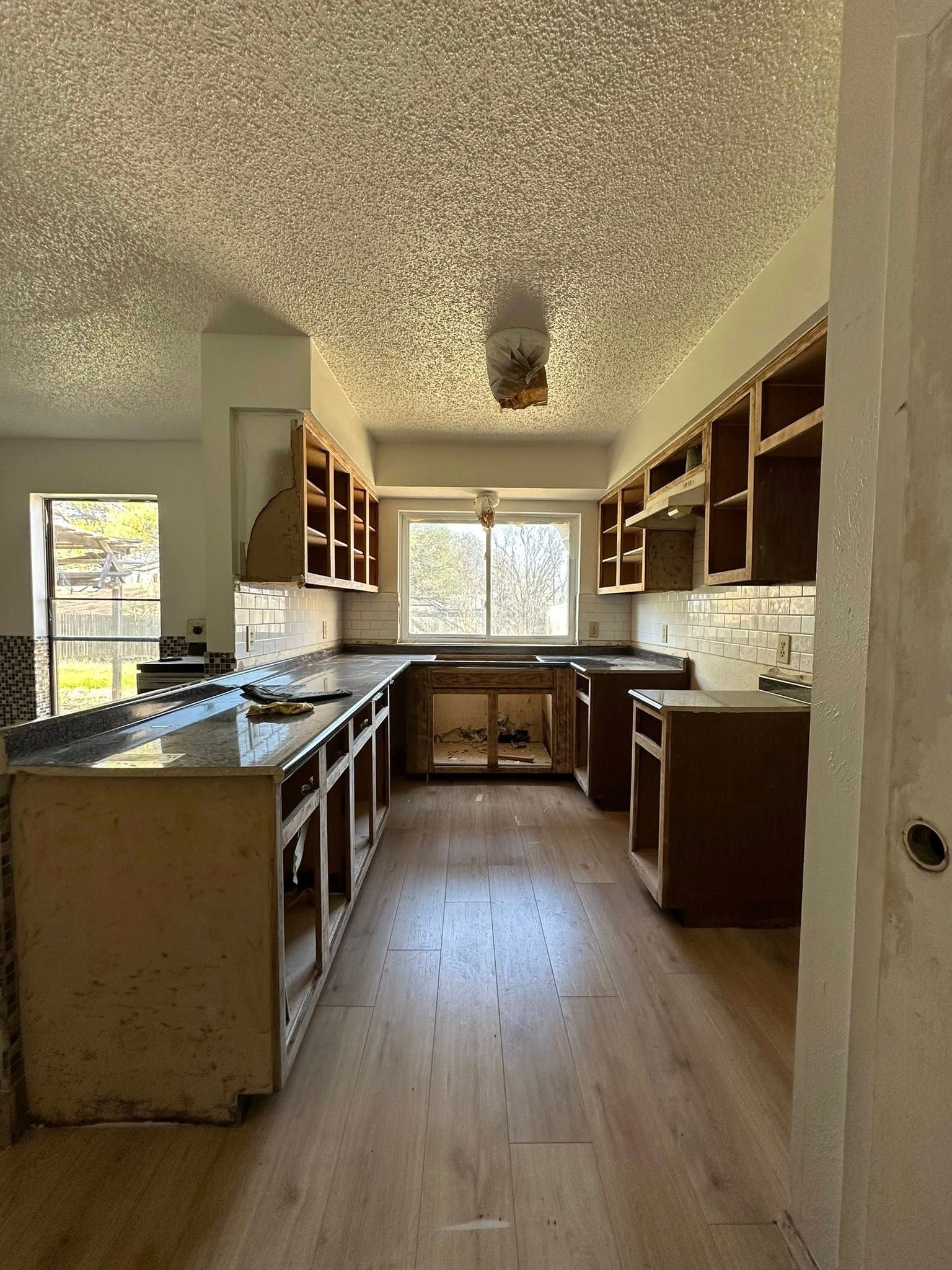 Kitchen undergoing renovation; wooden cabinets, countertops, and flooring are installed.