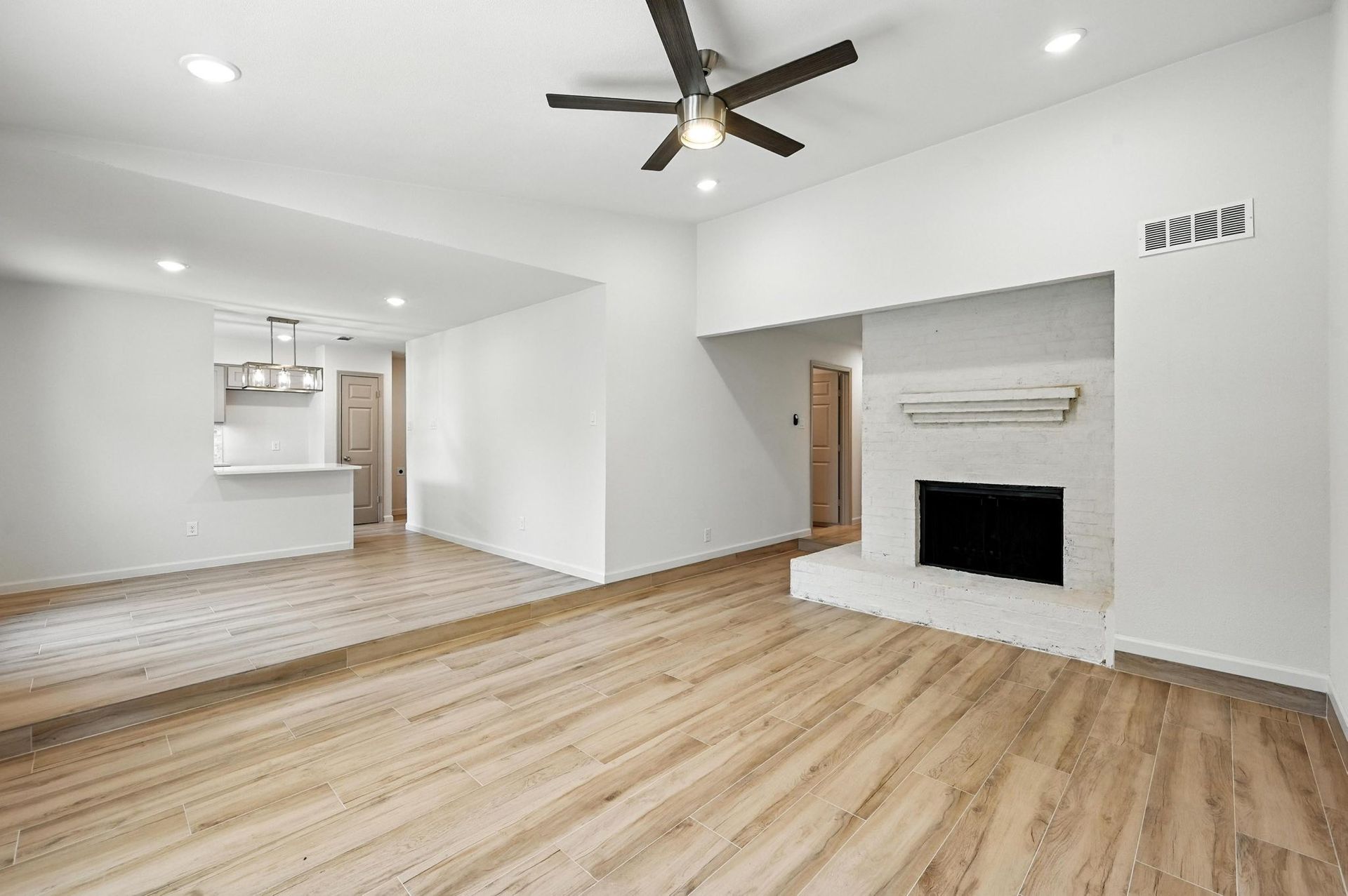 Bright living room with light wood floors, white walls, fireplace, and open kitchen.