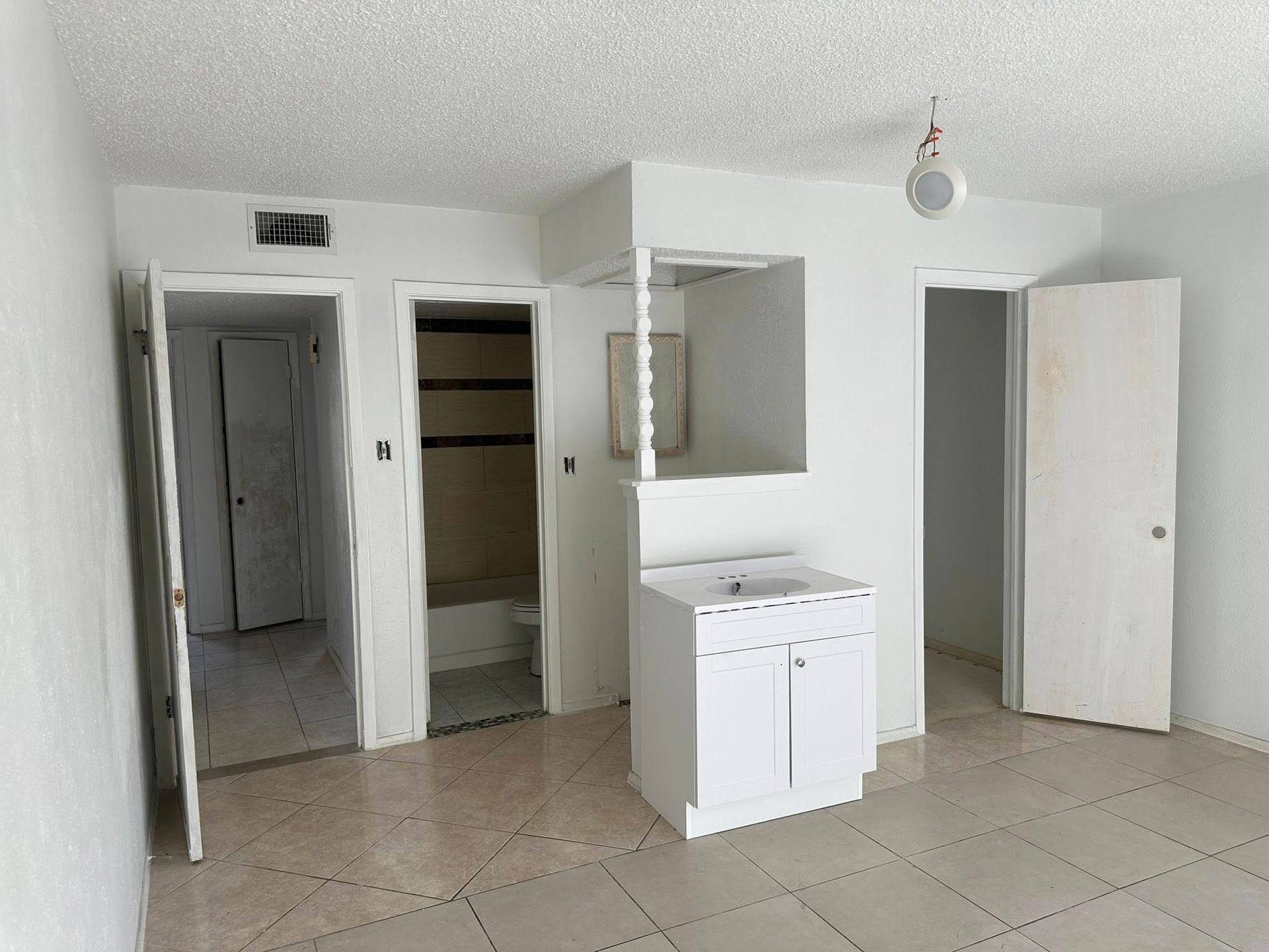 A small, empty interior room with white walls, tiled floor, and three doorways.