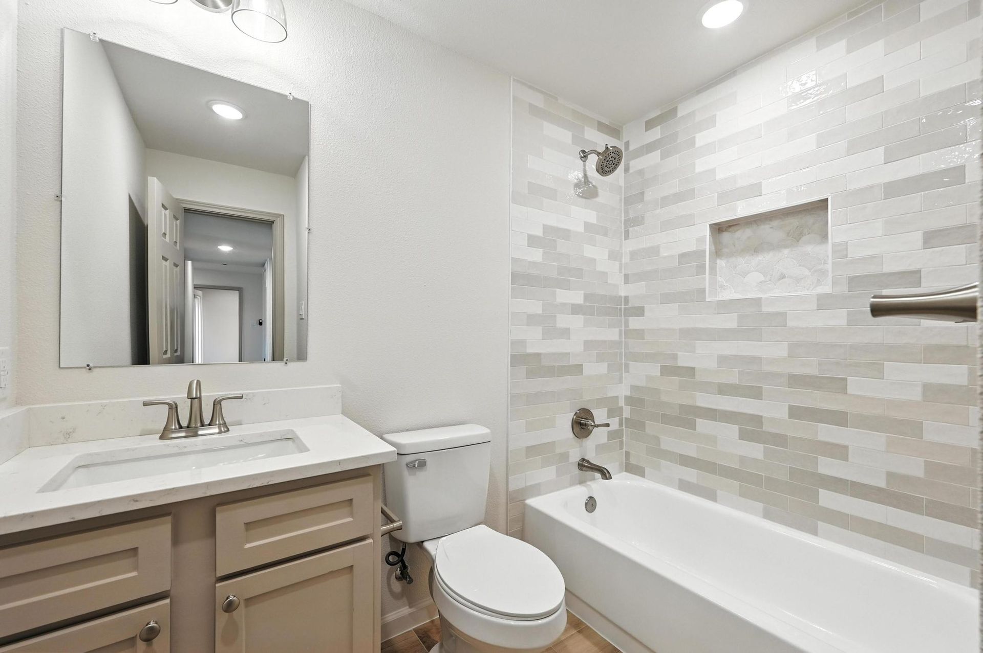 Bathroom with white and gray tiled shower, vanity, toilet, and a large mirror.