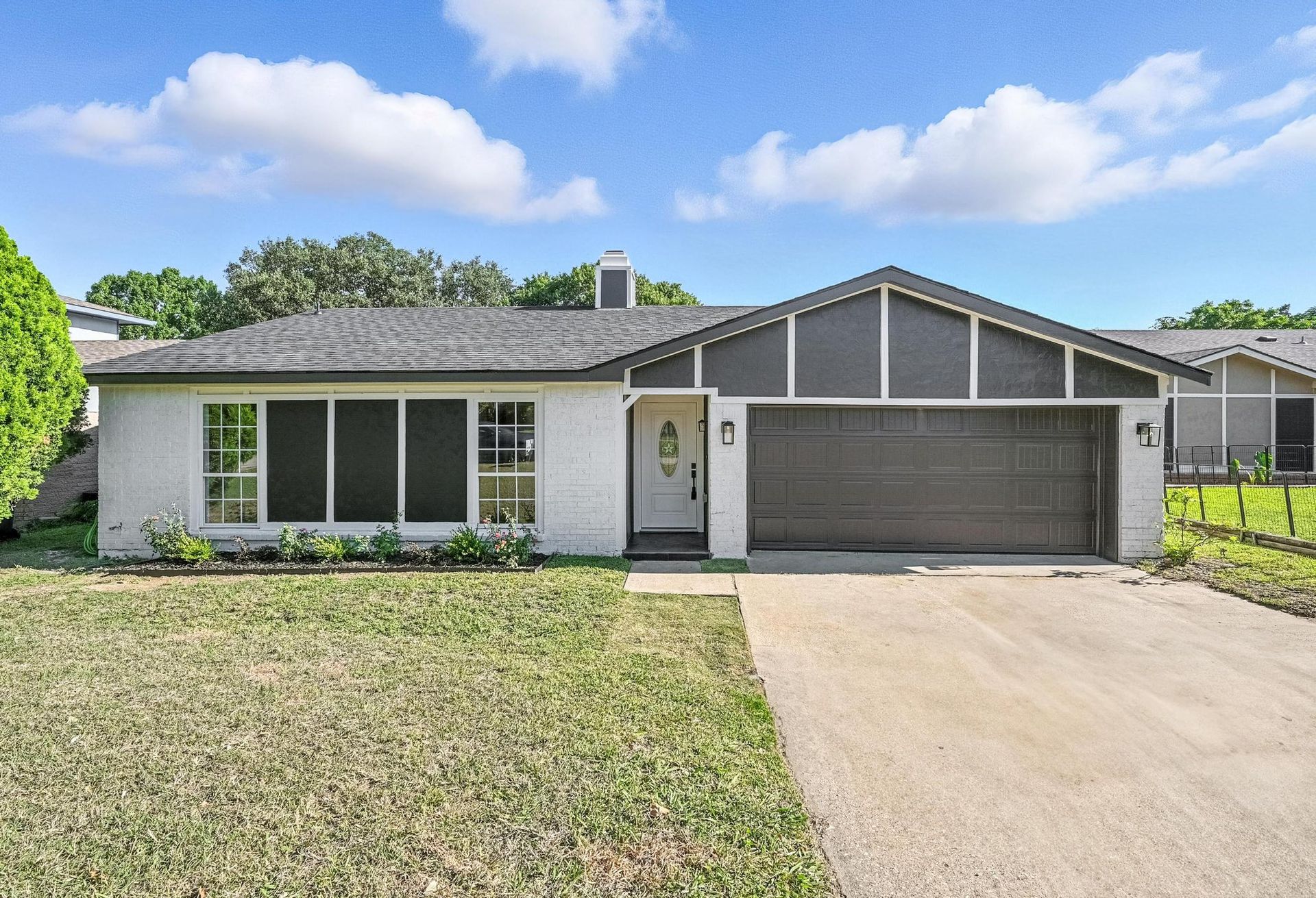 White ranch-style house with dark trim and a two-car garage under a blue sky with clouds.