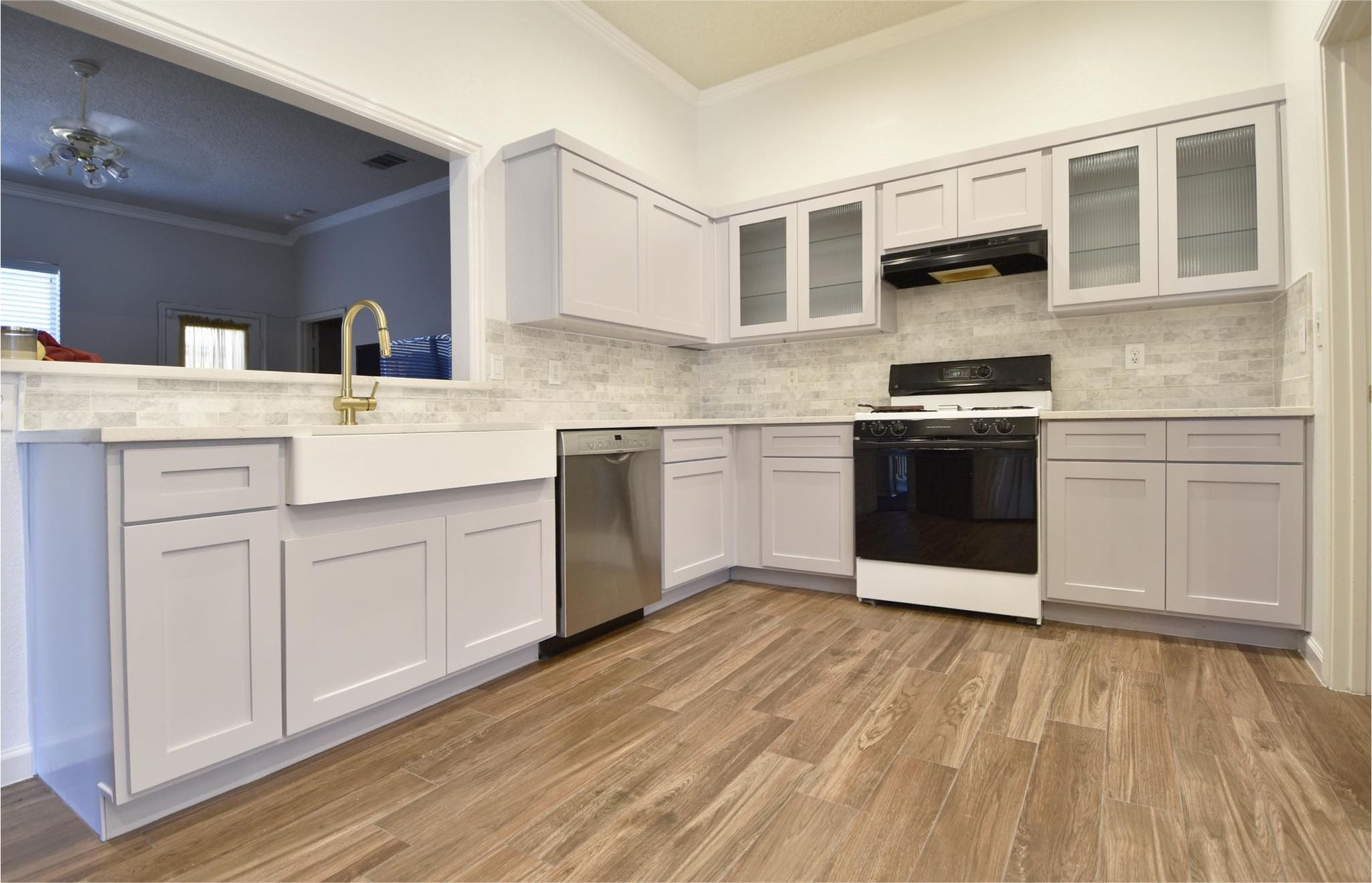 Modern kitchen with light gray cabinets, stainless steel appliances, and wood-look flooring.