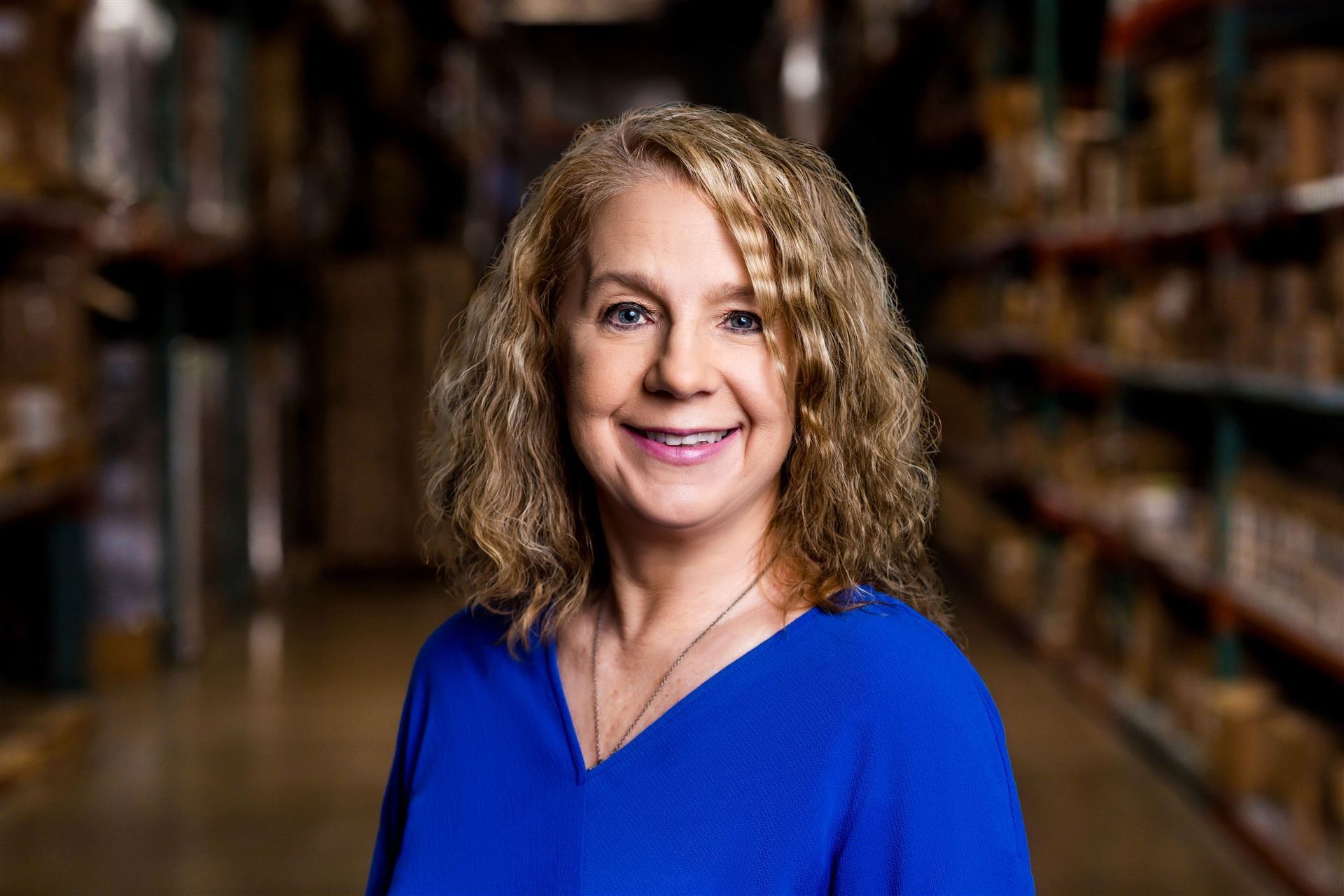 Smiling woman in a blue top standing in a store aisle with shelves in the background