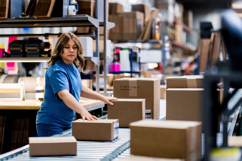 Worker in a blue shirt packing cardboard boxes in a warehouse on a conveyor belt