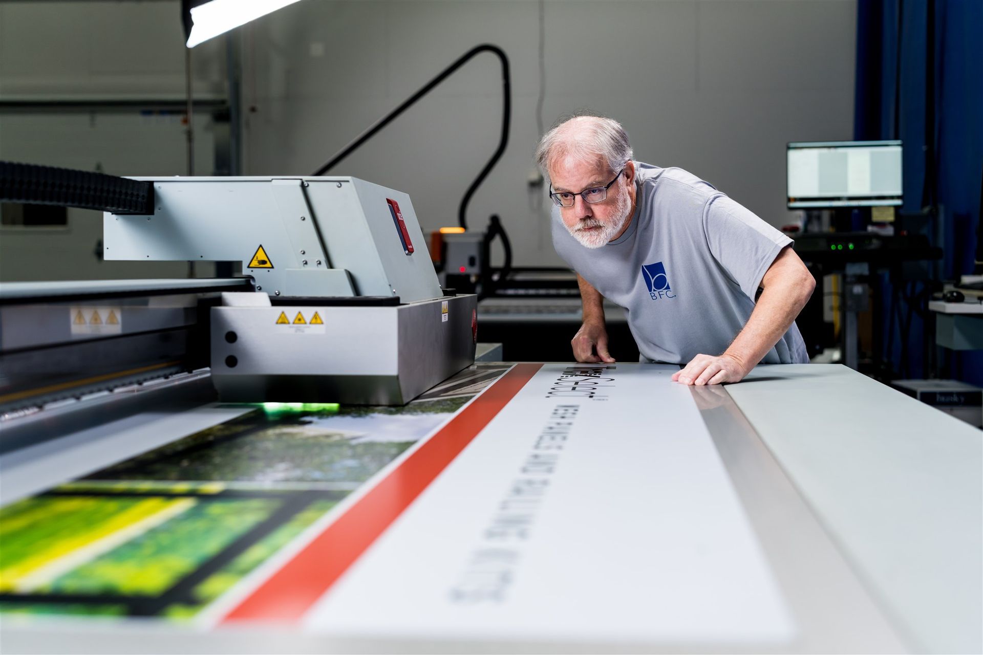 Man inspecting a large-format printer as it prints a colorful banner in a workshop