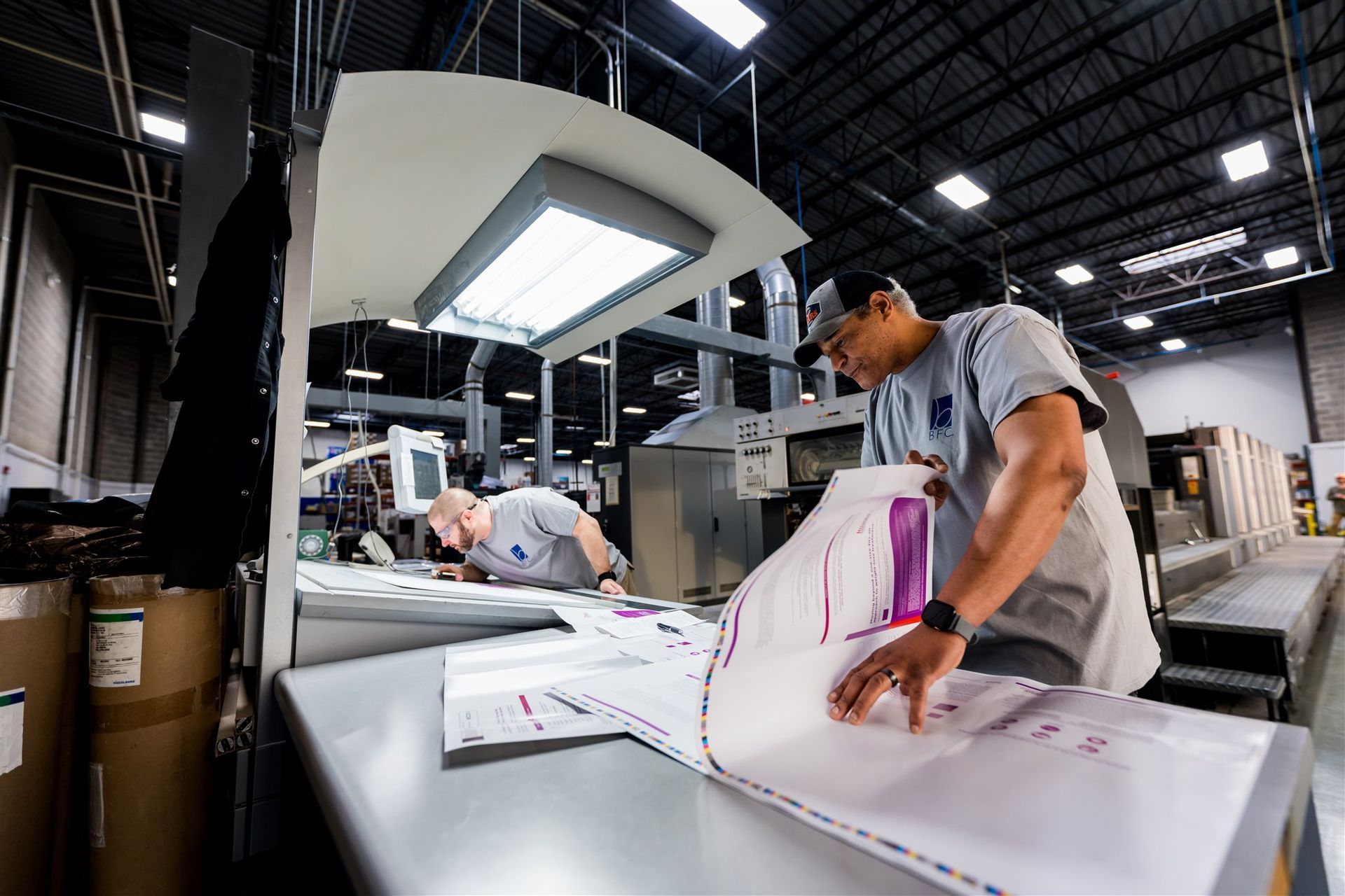Printing technician inspecting large sheets in a factory with bright overhead lights