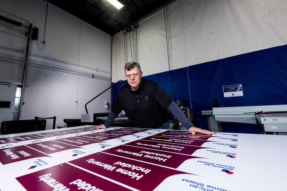 Person in a print shop leaning over a large sheet of burgundy posters on a printing press