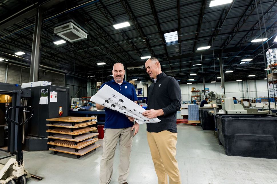 Two men in a factory examining a large blueprint together