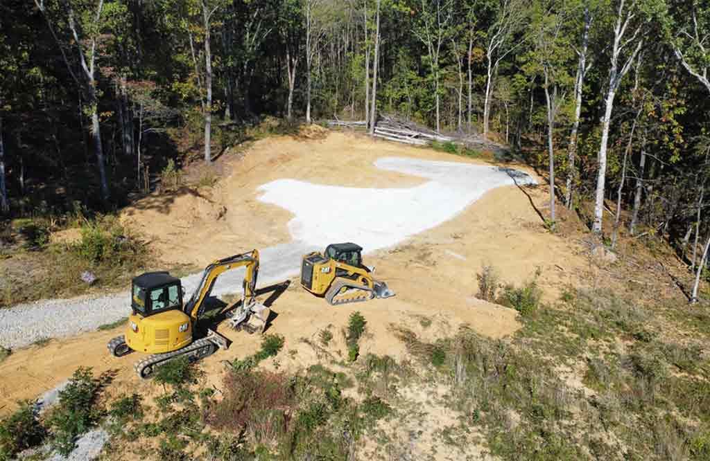 An aerial view of two bulldozers working on a dirt road in the woods.