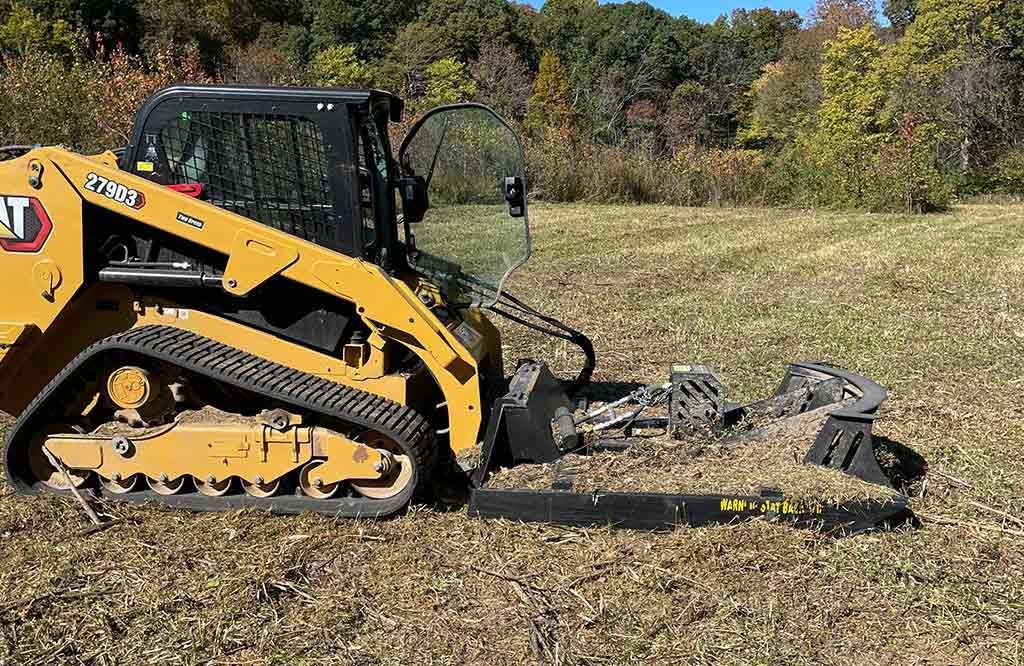 A bulldozer is cutting a tree stump in a field.