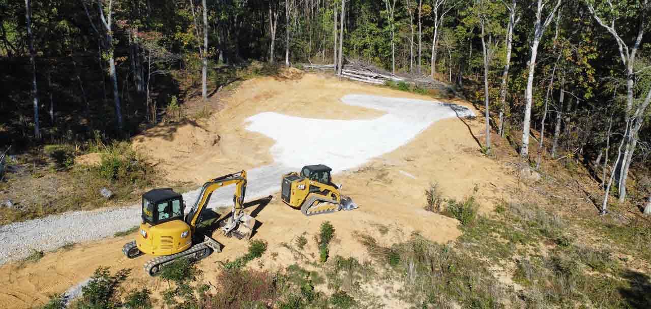 An aerial view of two bulldozers working on a dirt road in the woods.