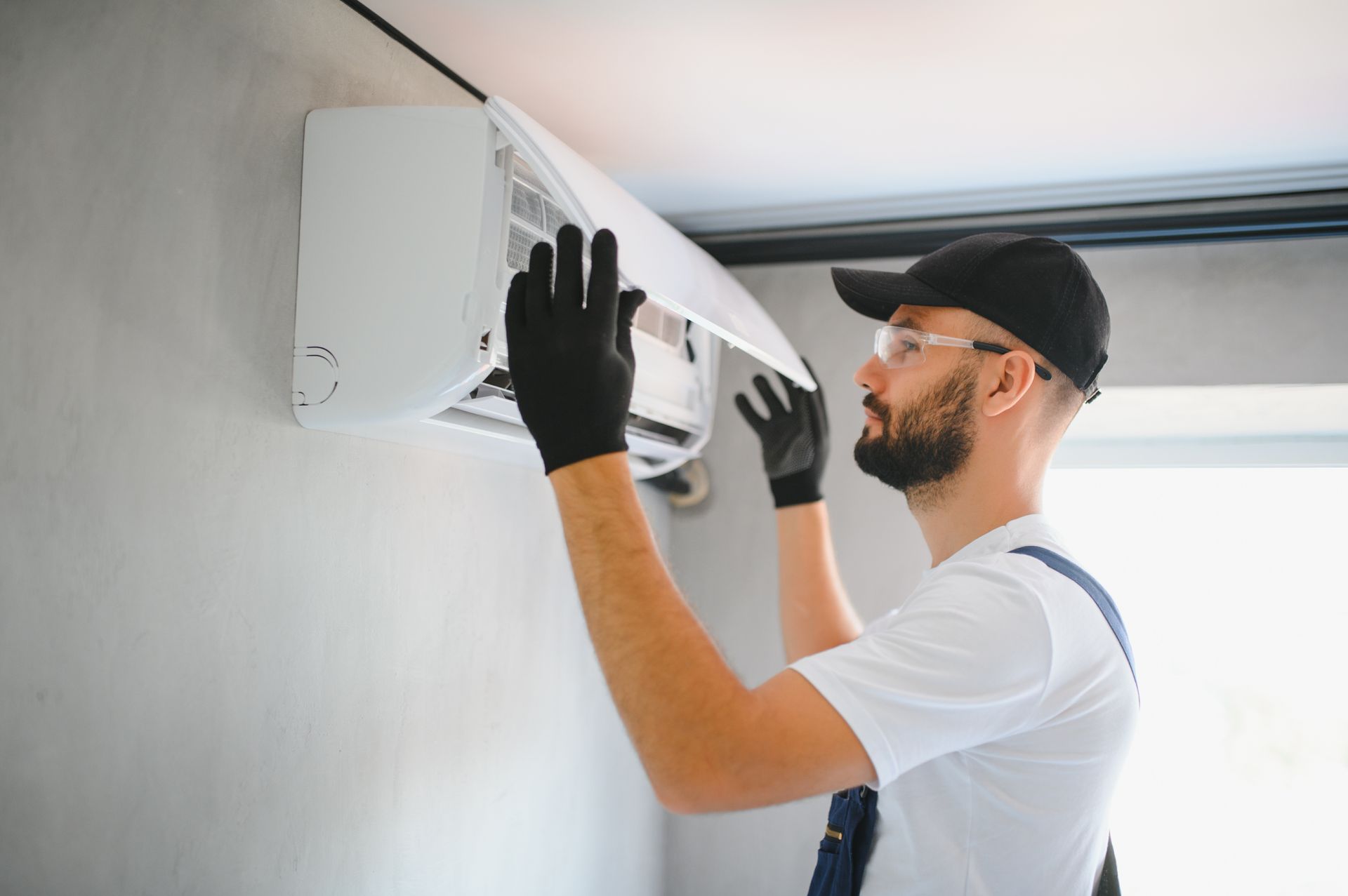 Person wearing gloves repairing or installing a wall-mounted air conditioning unit.