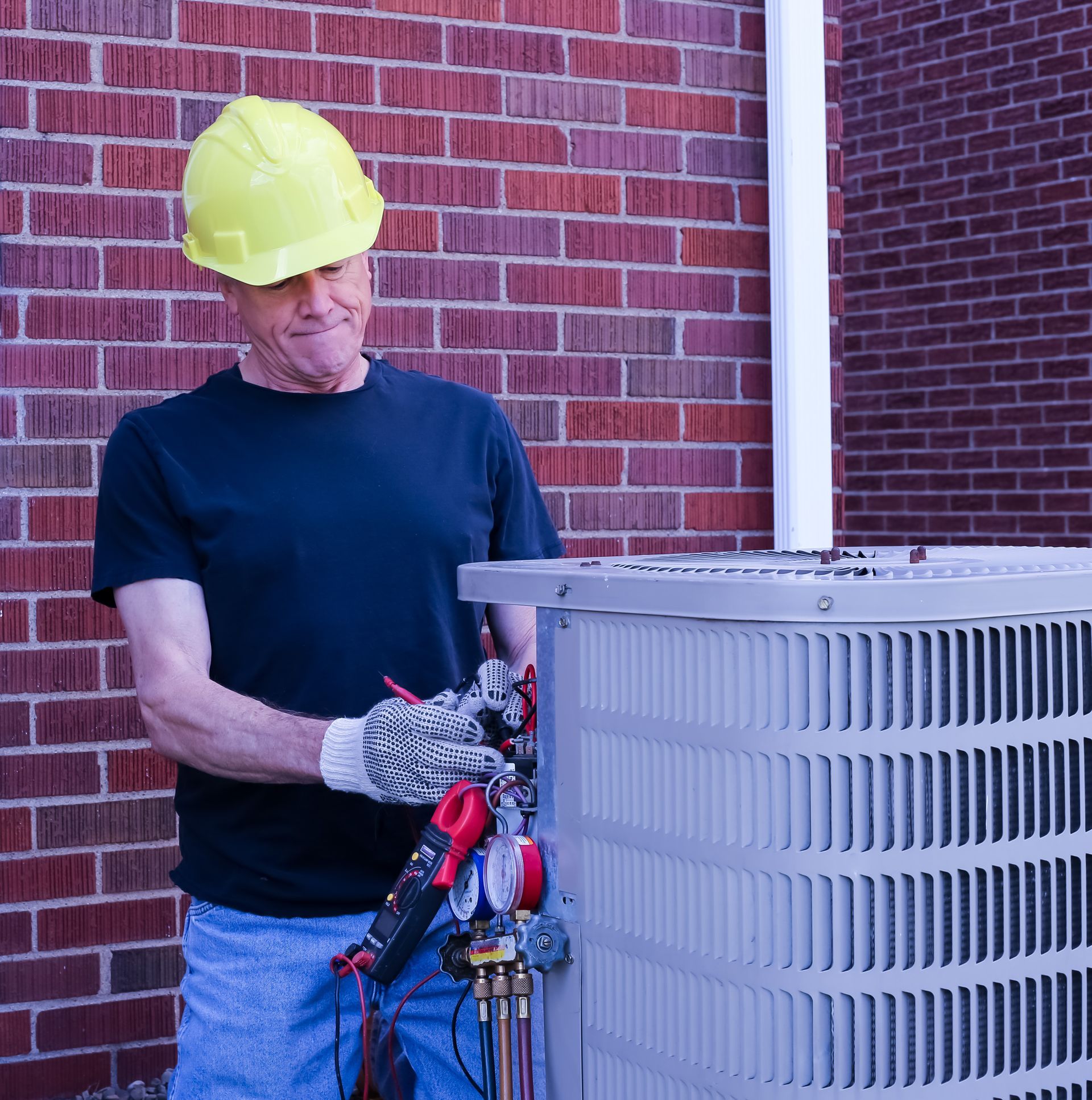 A professional HVAC technician installs an outdoor AC unit near a brick wall.