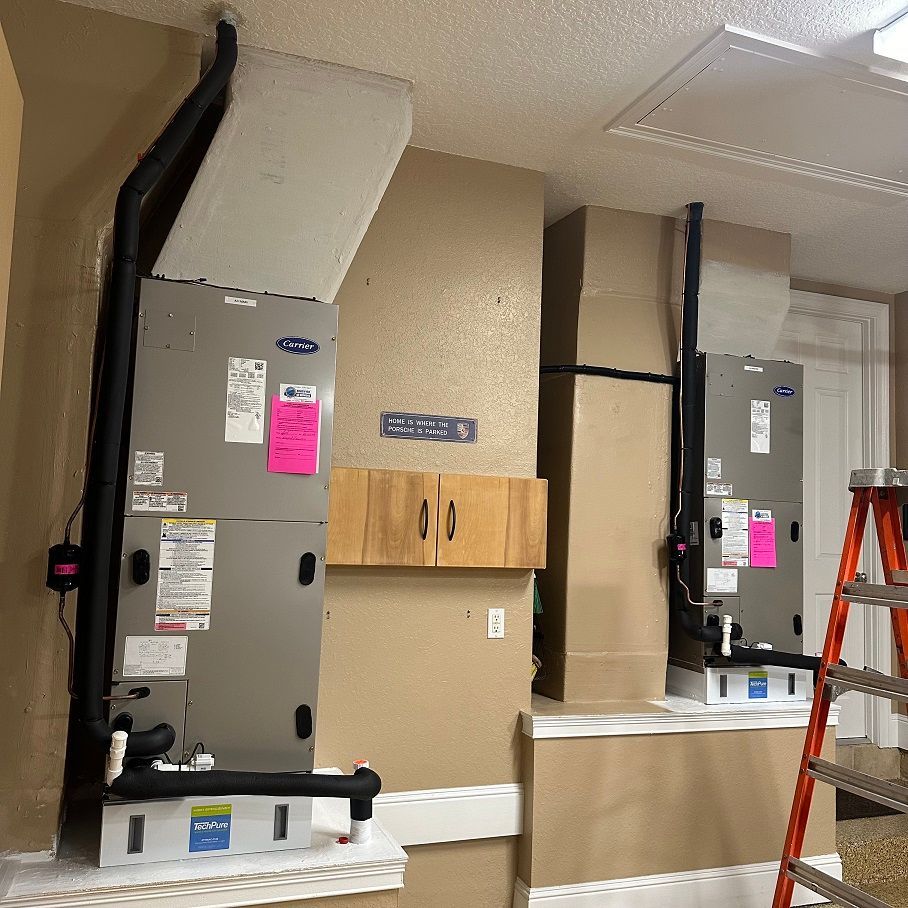 Two Carrier HVAC units installed in a wall with black ductwork, a small cabinet and a ladder nearby.
