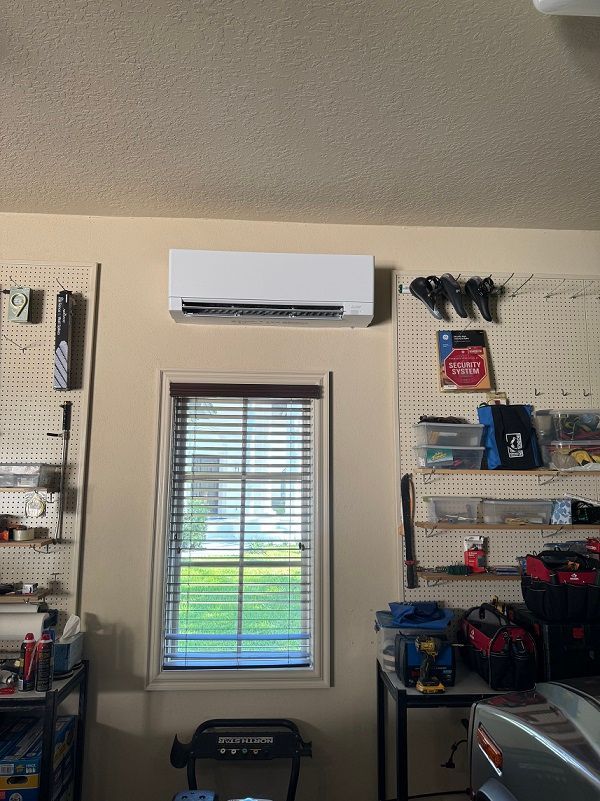 An air conditioning unit mounted above a window in a garage. Pegboards with tools are on either side.