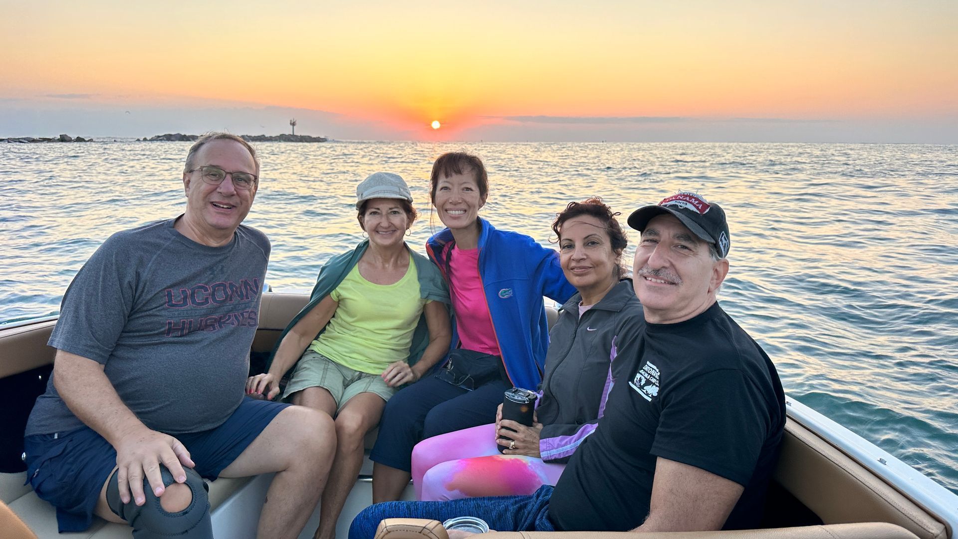 Five people on a boat at sunset on the water; the sun is low, casting an orange glow.