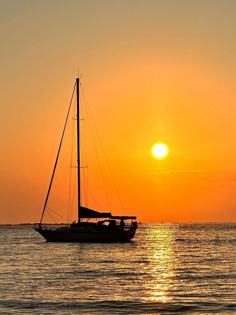 Sailboat silhouetted against a vibrant orange sunset over the ocean.