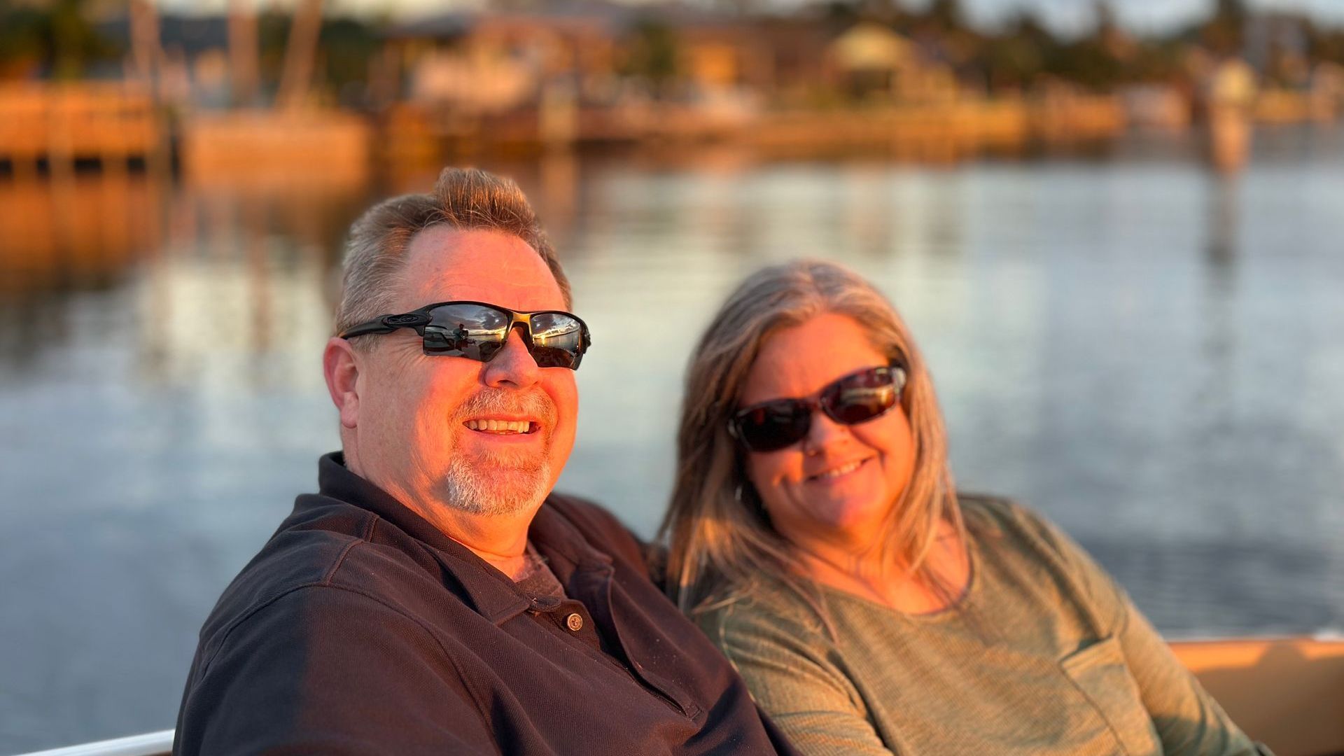 A smiling couple in sunglasses on a boat at sunset. 
