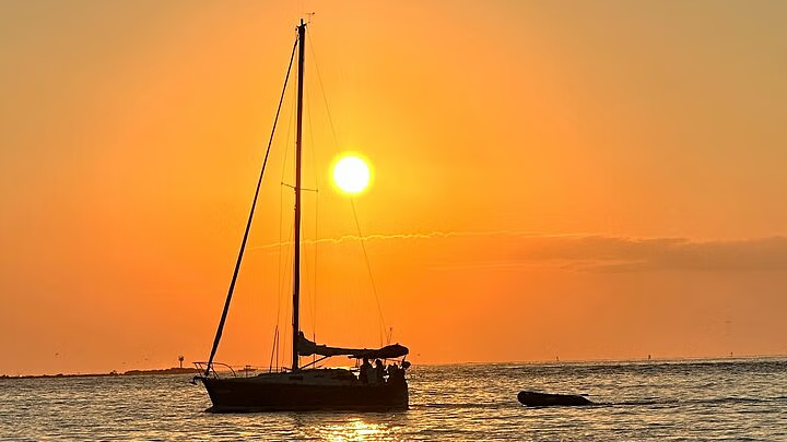 Sailboat silhouetted against a vibrant orange sunset over the water.