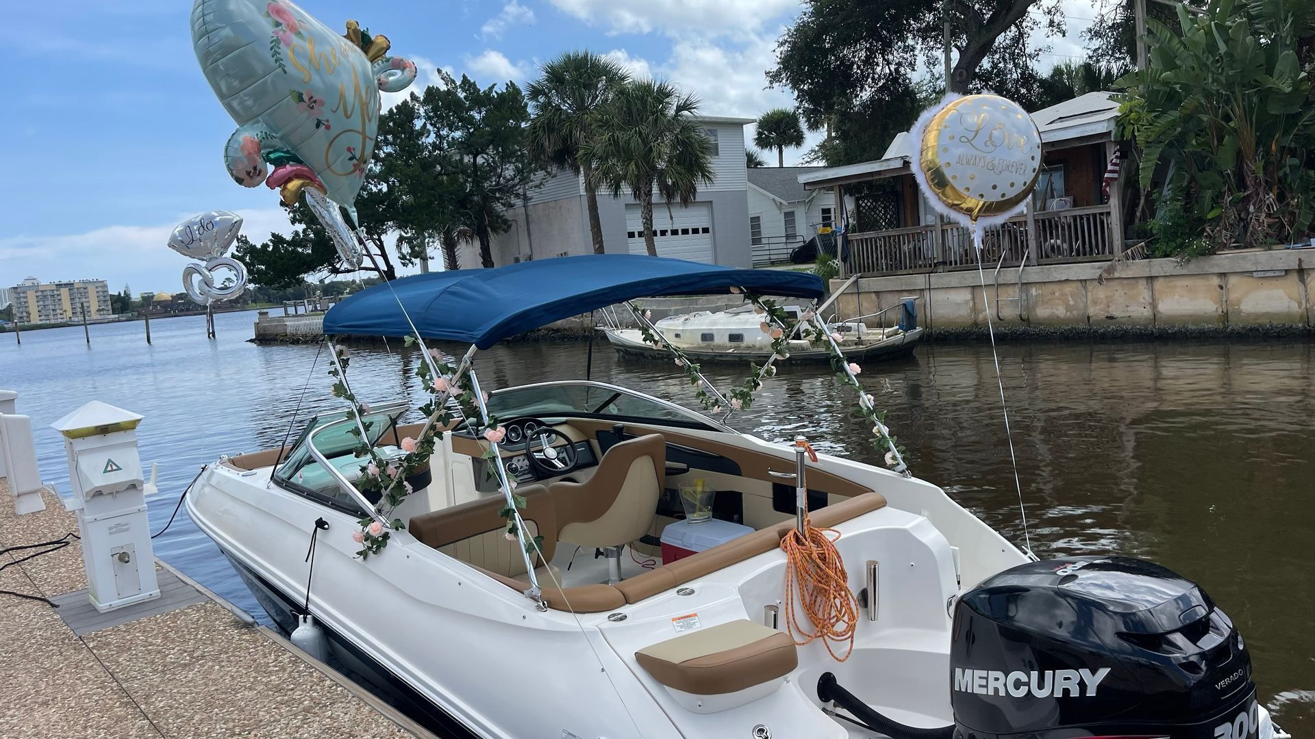 White motorboat docked in a canal, decorated with balloons.