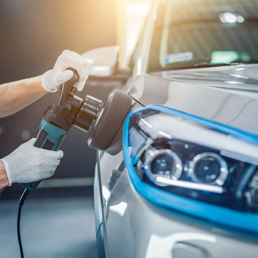 A person wearing gloves using a buffer on the front of a silver car, detail work in a garage.