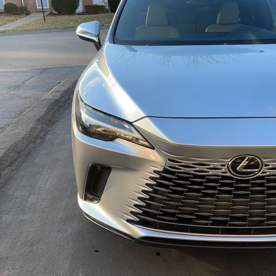 Silver Lexus SUV parked on a driveway with a textured front grille, daytime.