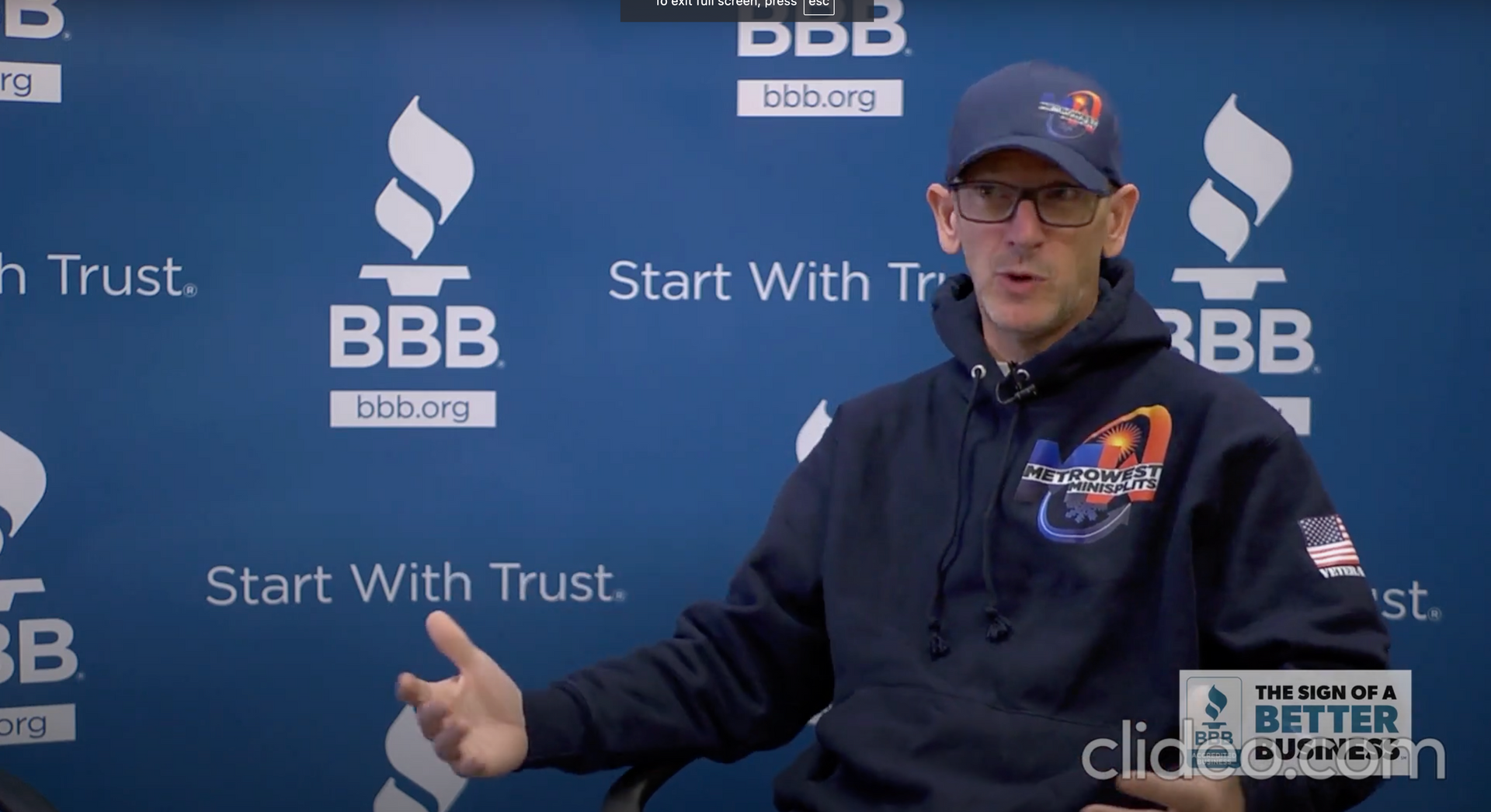 A man is sitting in front of a wall that says bbb