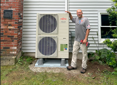 A man is standing in front of a large air conditioner on the side of a house.