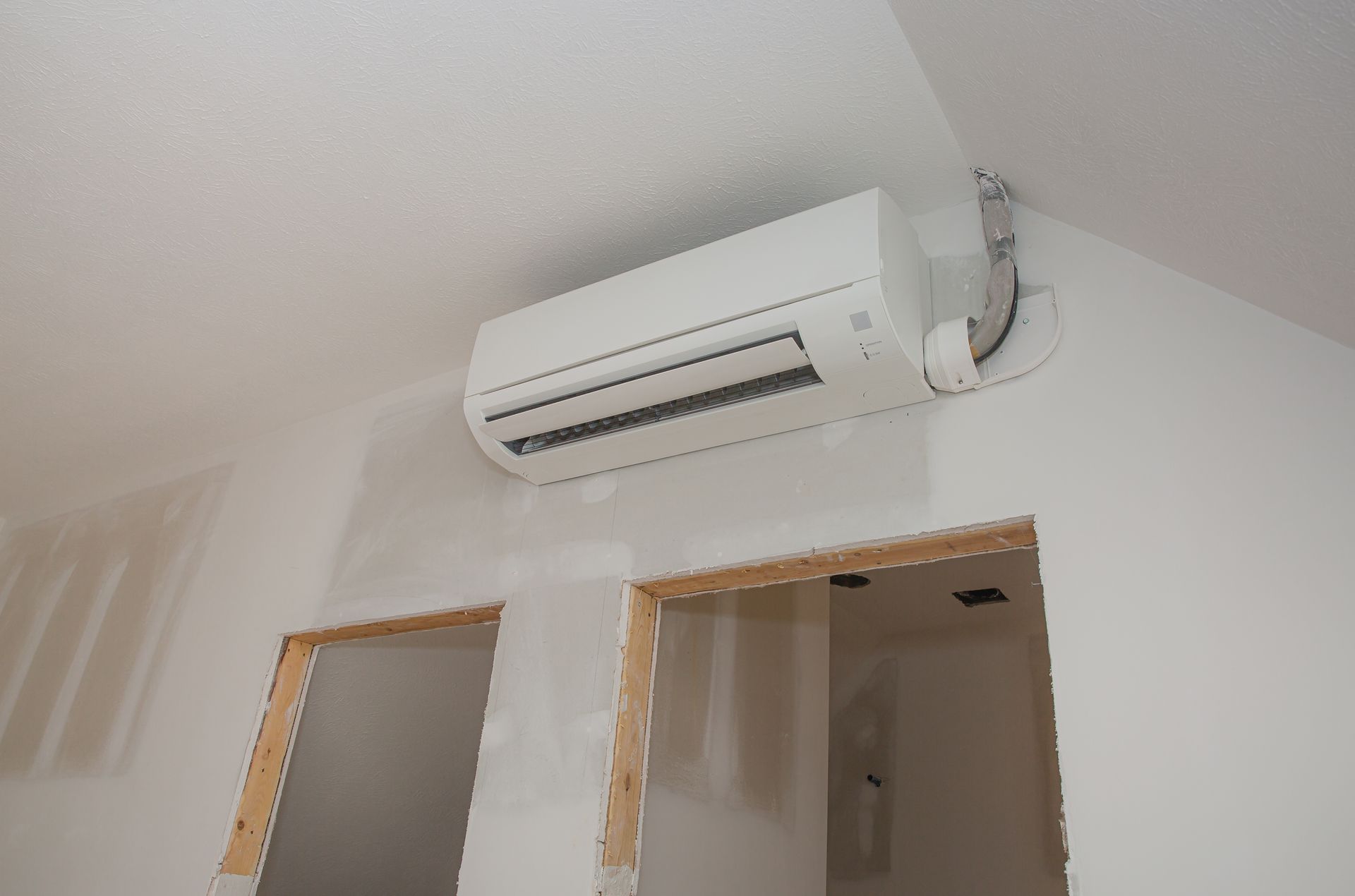 White air conditioning unit mounted on a white wall in a room under construction.