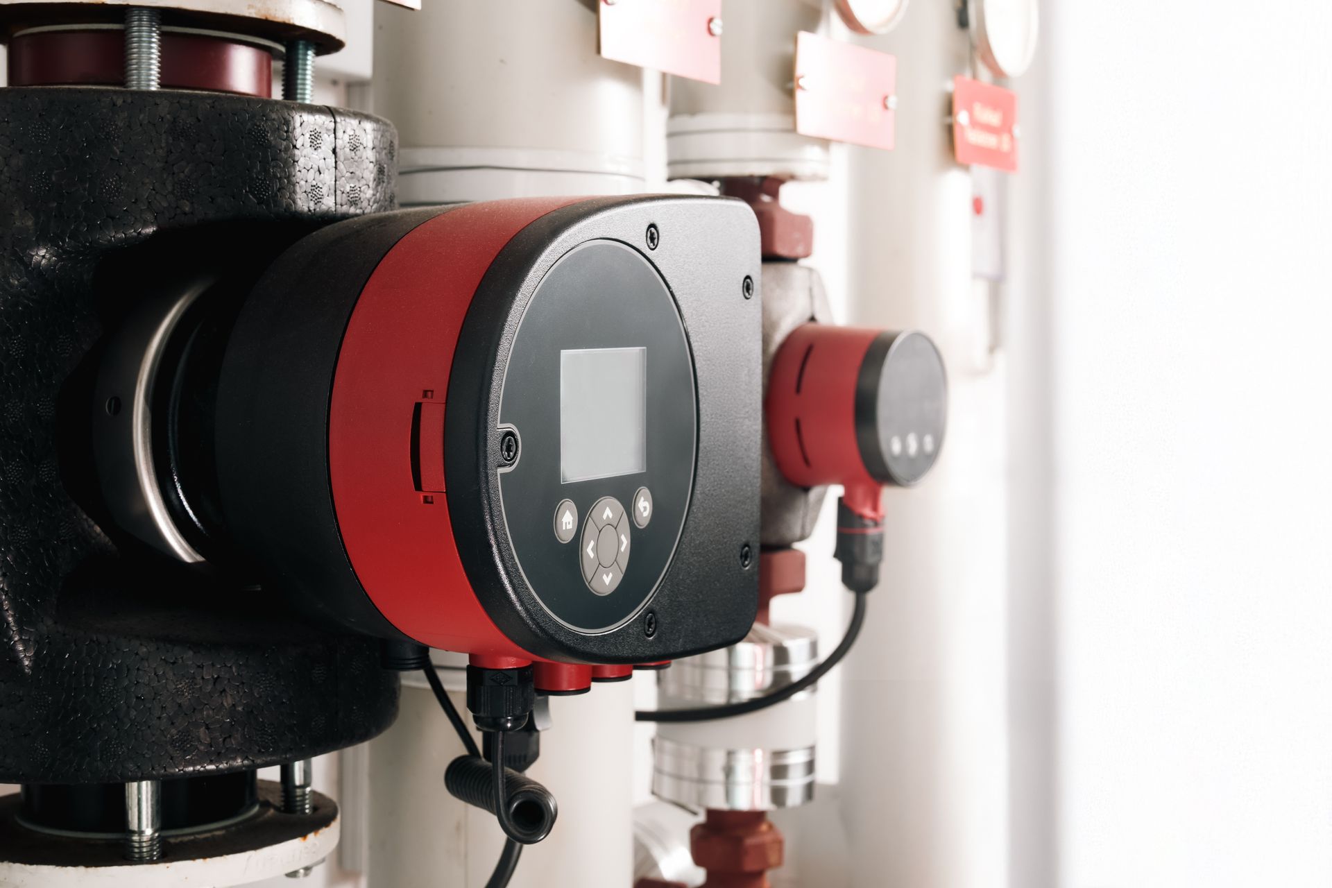 Black and red water pump with a digital display, attached to white pipes in an industrial setting.