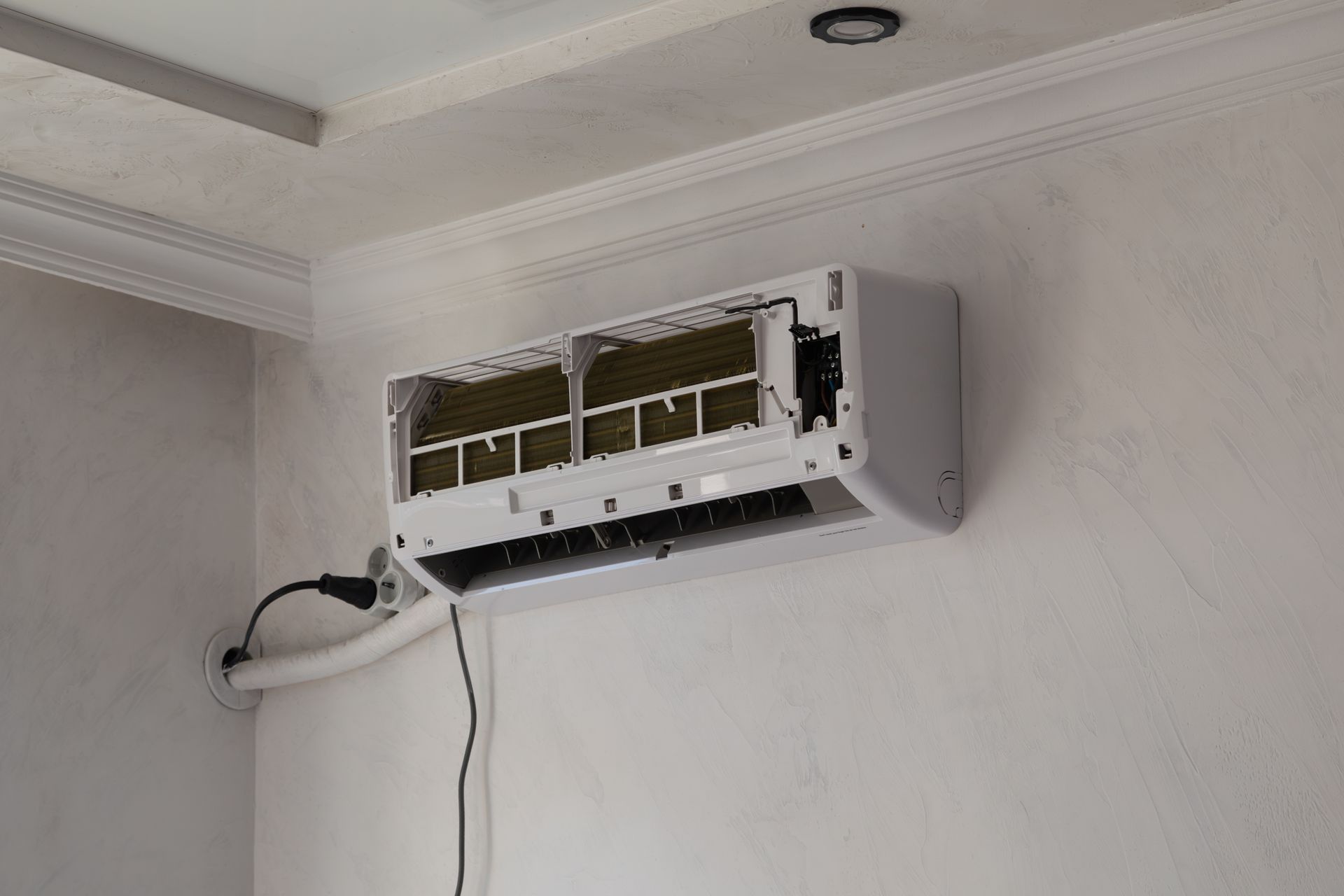 White air conditioning unit mounted on a white wall, with exposed interior and black power cord.