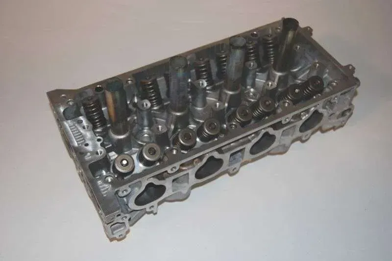 A close up of a cylinder head on a white surface.