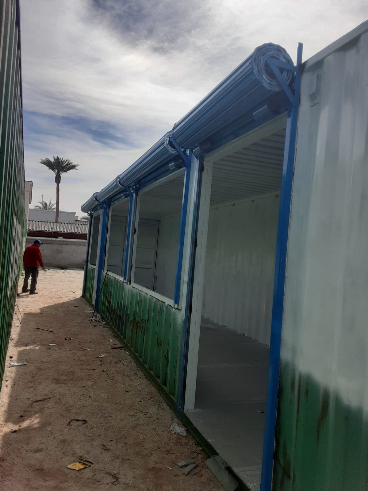 Un hombre con una chaqueta roja camina por un camino de tierra entre dos edificios.