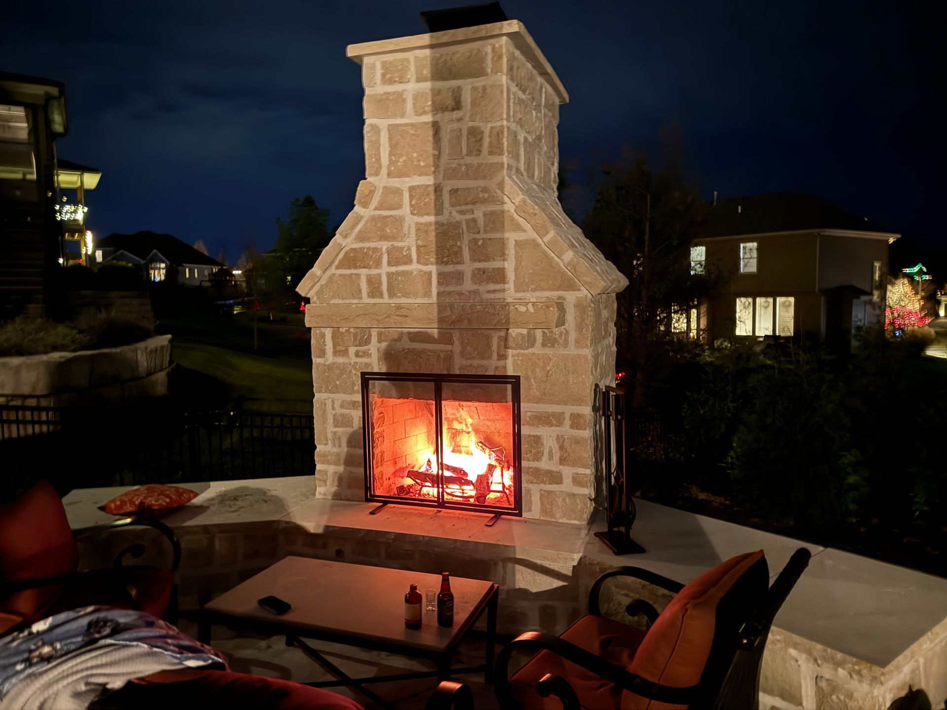 A fireplace is lit up at night in a backyard