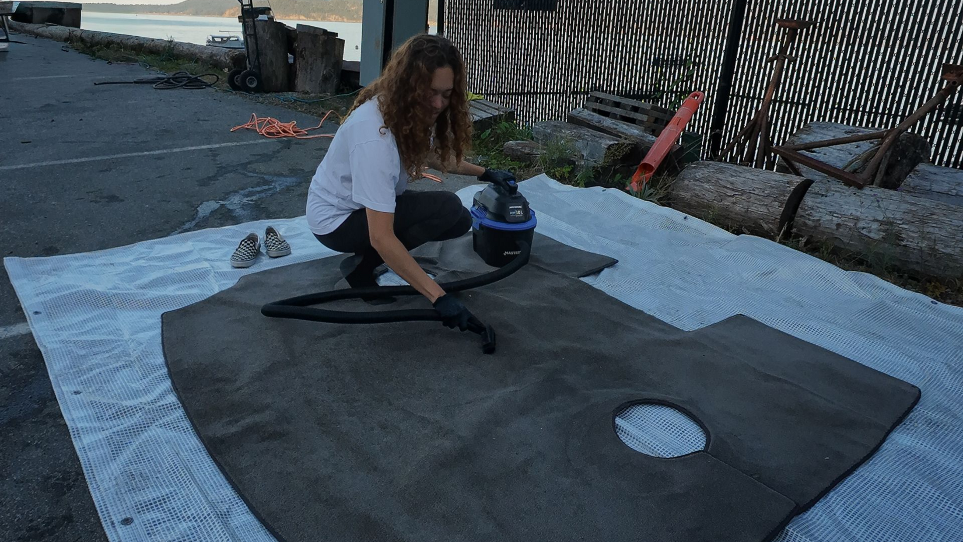 A person kneels, cleaning a car dashboard with a vacuum outside.