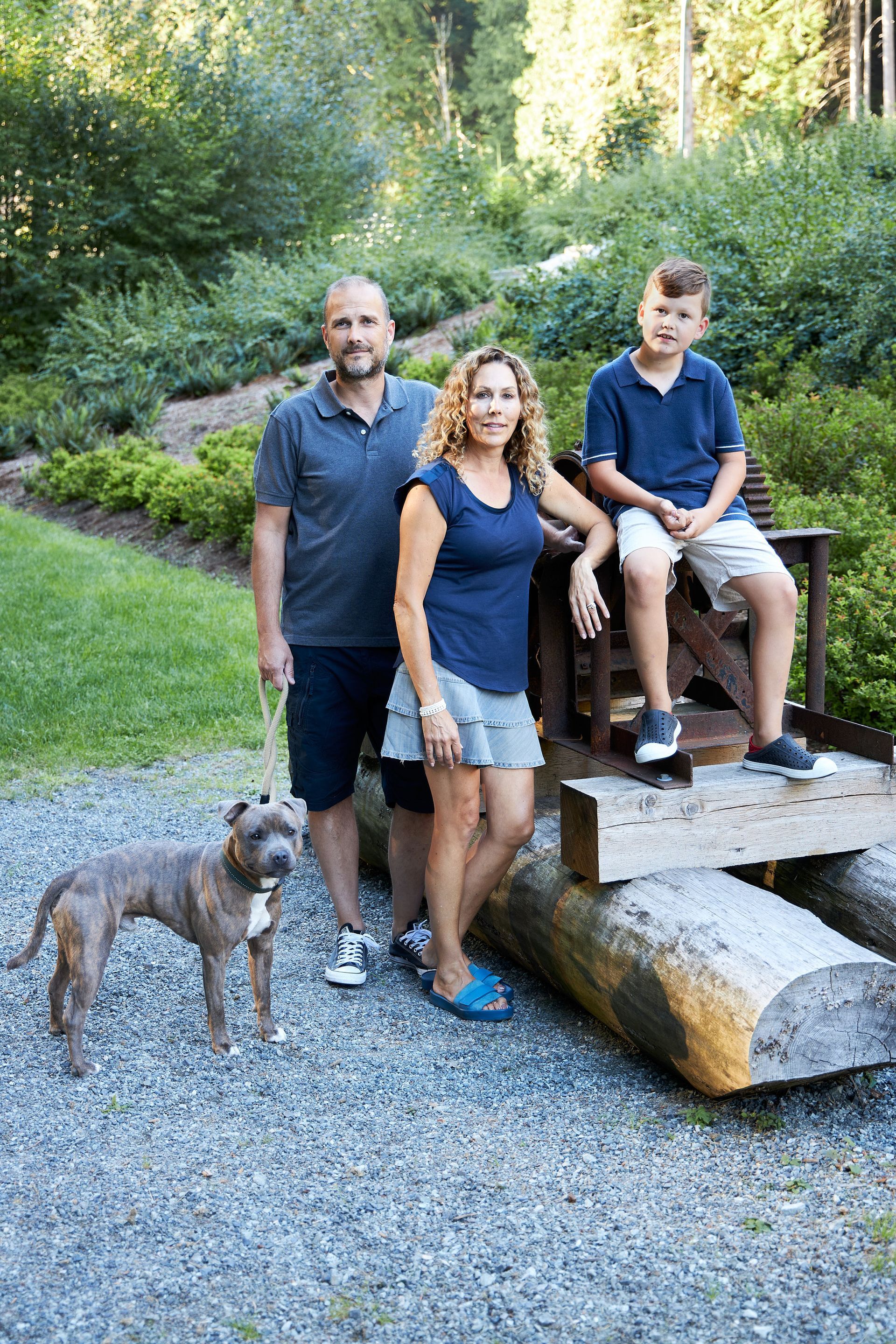 Family stands with dog near a wooden structure outdoors.